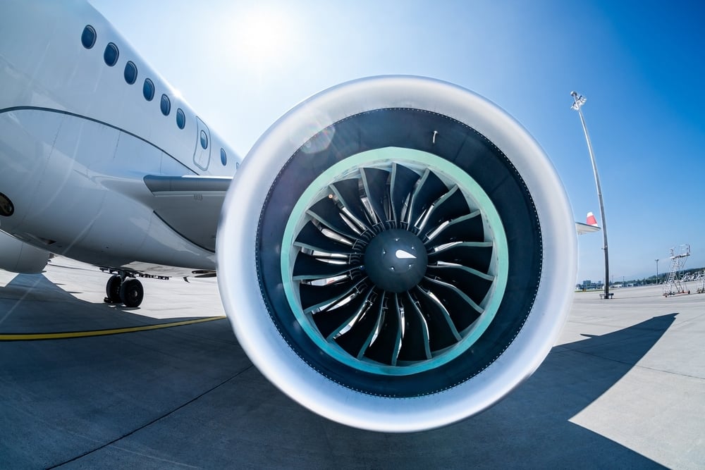 Close up of the wing engine of an airplane. Behind the plane is clear blue skies with the reflection of bright sunshine.